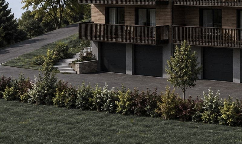 Gli spazi esterni a livello dello zoccolo: le porte dei garage scure, la rampa d'accesso, le scale in pietra e le aiuole che costeggiano il piazzale.