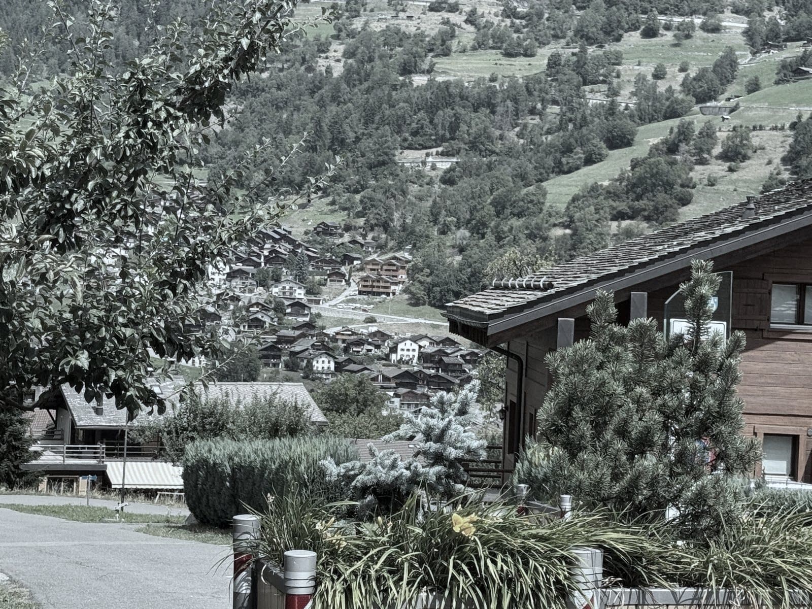 Un chemin des hauts du village, un chalet récent au premier plan et les toits en contrebas.