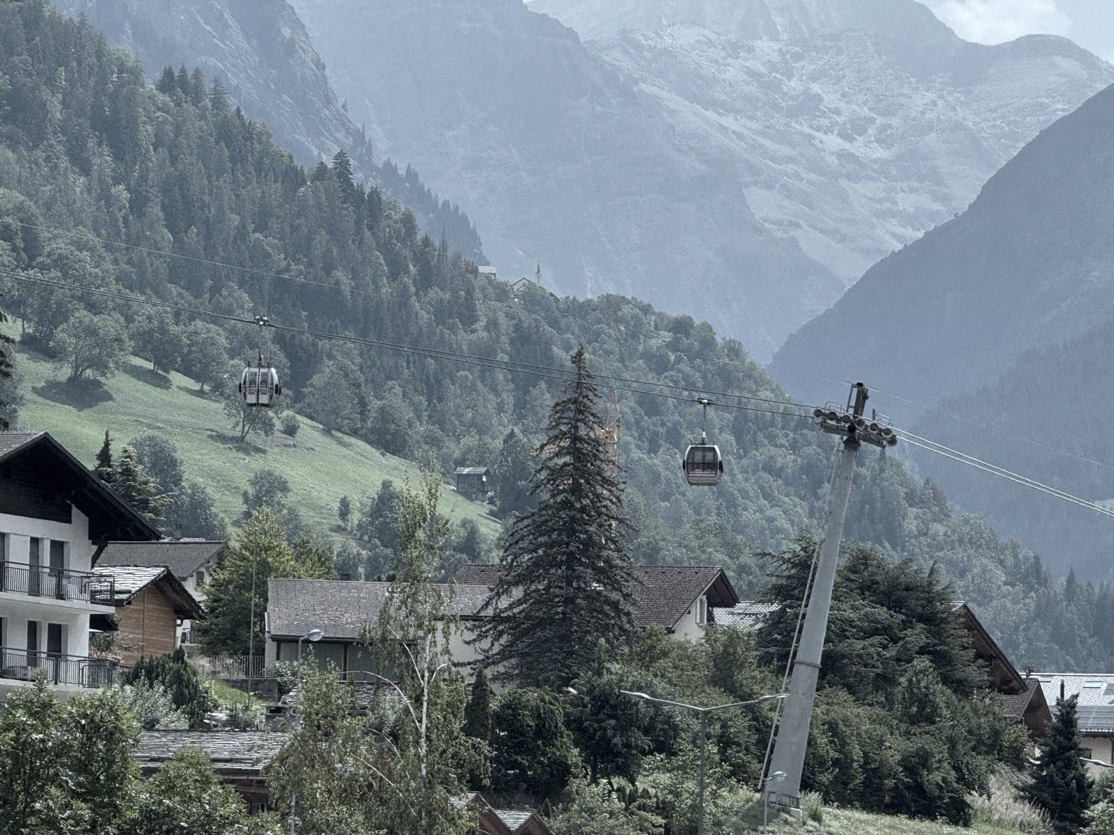 La cabinovia di Le Châble sopra i tetti, due cabine si incrociano sullo sfondo dei versanti boscosi.
